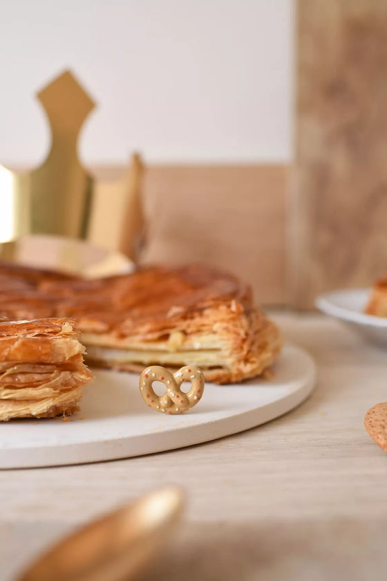 Fève Bretzel Baubels en porcelaine artisanale beige et dorée sur carte Les Jolies Fèves