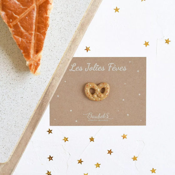 Fève Bretzel Baubels en porcelaine artisanale beige et dorée sur carte Les Jolies Fèves