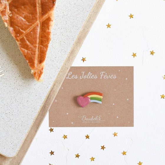 Fève Cœur Filant Baubels en porcelaine artisanale avec arc-en-ciel et cœur rose sur carte Les Jolies Fèves